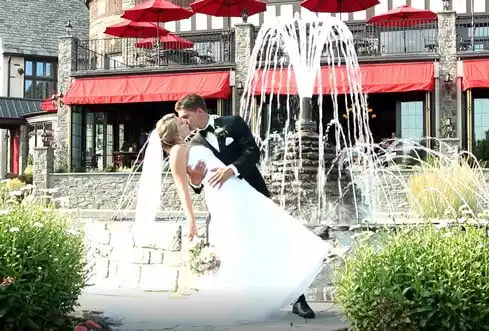 Groom holding bride and kissing her in front of a fountain