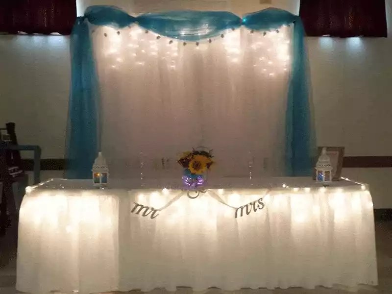 Head table in white with uplights and blue swag lighted curtain backdrop