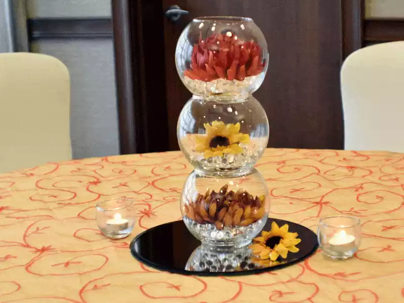 Stacked glass fishbowls with crystals and fall flowers on glass mirror centerpiece