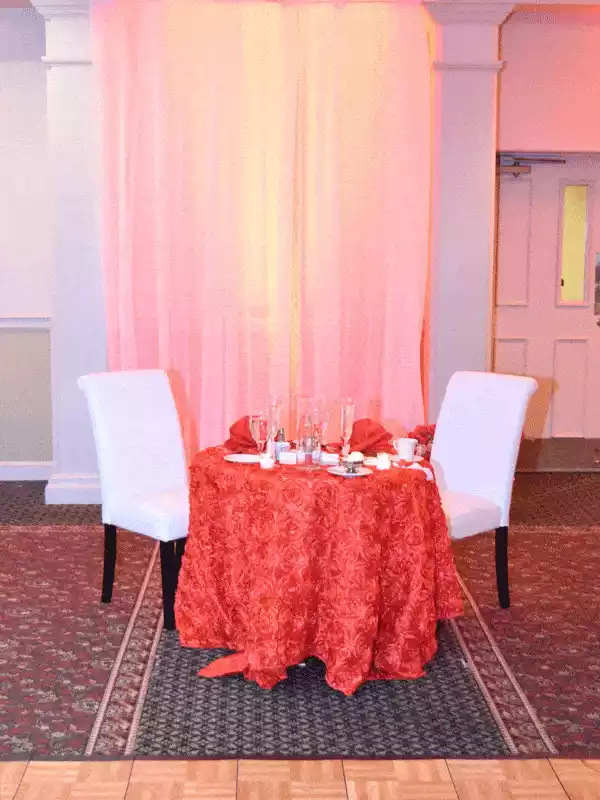 Seating for guest of honor at a quinceanera coral rosette table cloth and drapery with uplighting