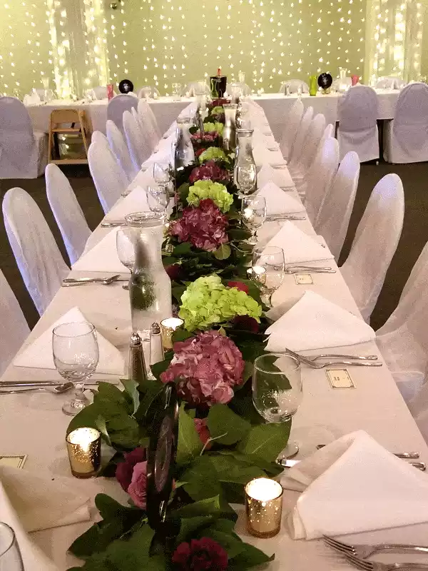 Long floral garland set on white table linens with light curtain backdrop