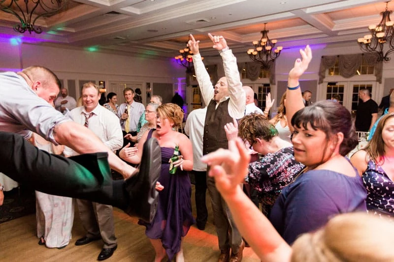 A surprised woman reacting to a man jumping in the air and doing a split at a wedding reception