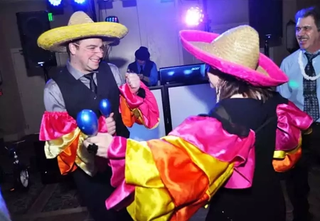 A man and a woman dressed in conga sleeves shaking maracas in a conga line dance