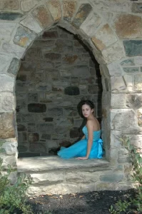 Girl in a teal dress sitting in a stone window opening