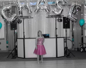 Black and white photo with a pop of color of a young woman standing in front of the DJ booth at her bat mitzvah