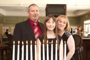 Girl and her parents standing behind a candelabra for her candle lighting at her bat mitzvah