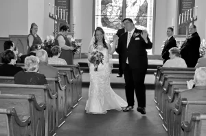 Black and white photo of groom dancing his way up the aisle with his new bride