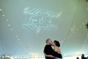 Bride and groom kissing under wedding tent with their monogram above them