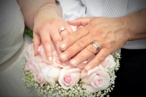 Bride and groom hands on top of floral bouquet showing their wedding rings