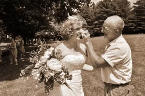 A sepia photo of a dad wiping a tear from the eye of his daughter the bride