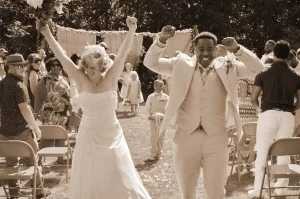A sepia photo of a bride and groom cheering as they walk up the aisle after being married