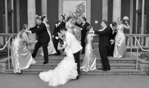 A black and white photo of a bridal party fighting while the bride and groom are kissing
