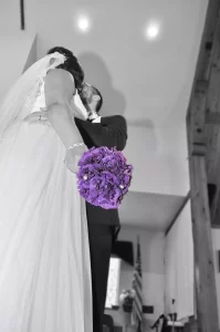 A black and white photo of a bride groom with a purple colored floral bouquet
