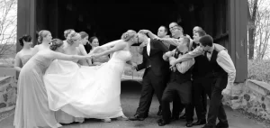 Black and white photo of a couple kissing and their bridal party trying to pull them apart