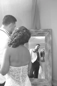 A black and white photo of a bride and groom looking at themselves in a mirror