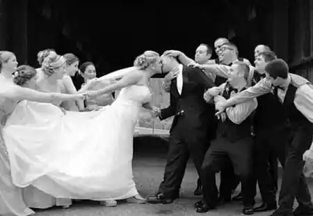 Bridal party pulling bride and groom apart during a kiss